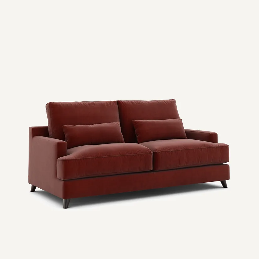 Canapé Alwine rouge brique en velours, vu de trois quarts, avec deux coussins et pieds fuselés.